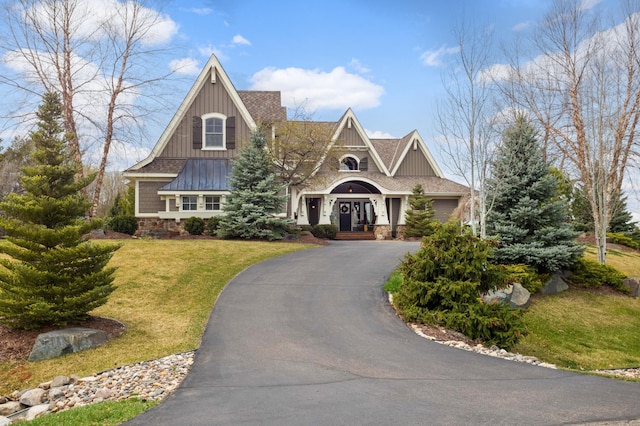 view of front of house featuring aphalt driveway, french doors, board and batten siding, stone siding, and a front lawn