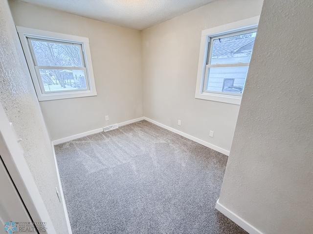 carpeted empty room featuring visible vents, baseboards, a wealth of natural light, and a textured wall