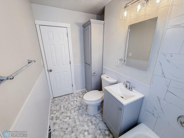 full bath with a bathtub, a textured ceiling, toilet, and vanity