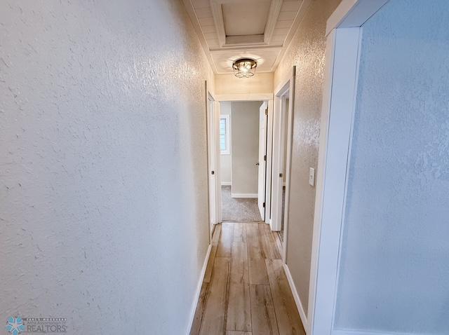 corridor featuring baseboards, wood finished floors, and a textured wall