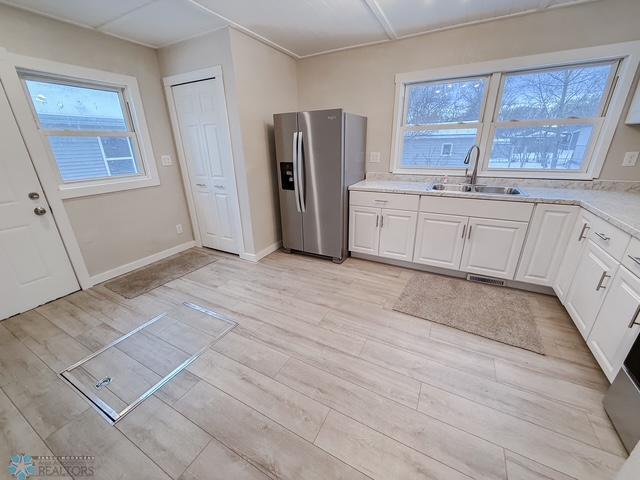 kitchen featuring light wood-style flooring, light countertops, white cabinetry, stainless steel refrigerator with ice dispenser, and a sink