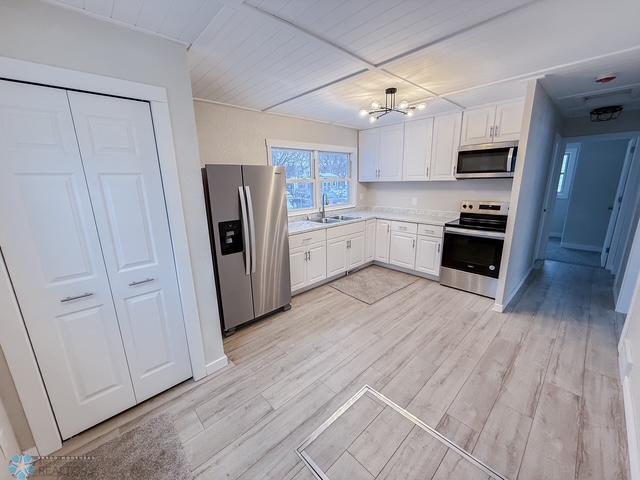 kitchen featuring appliances with stainless steel finishes, a sink, light wood-style flooring, and white cabinetry