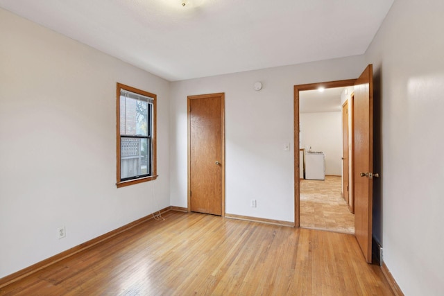 unfurnished bedroom featuring washer / dryer, a closet, baseboards, and light wood finished floors