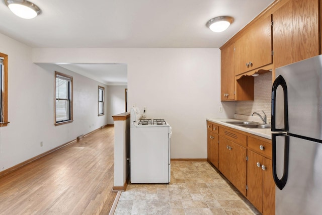 kitchen with washer / dryer, brown cabinetry, freestanding refrigerator, light countertops, and a sink