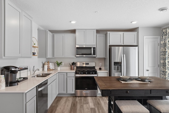 kitchen featuring a textured ceiling, stainless steel appliances, a sink, light wood-style floors, and light countertops