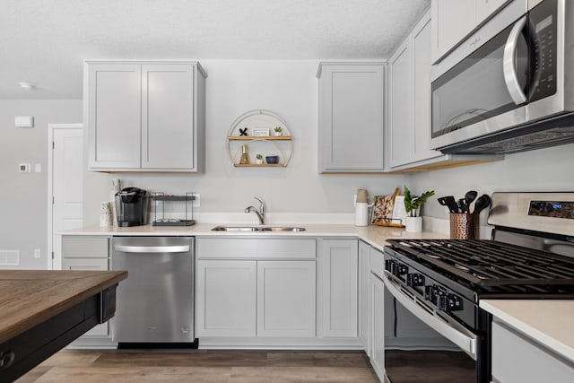 kitchen with a textured ceiling, appliances with stainless steel finishes, light countertops, and a sink