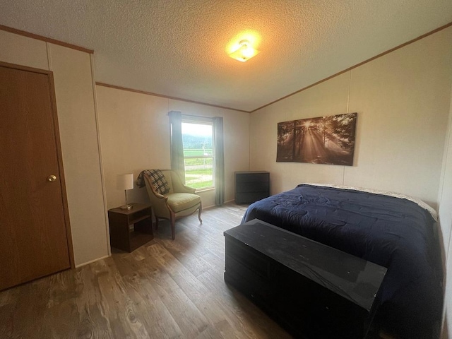 bedroom featuring a textured ceiling, vaulted ceiling, crown molding, and wood finished floors