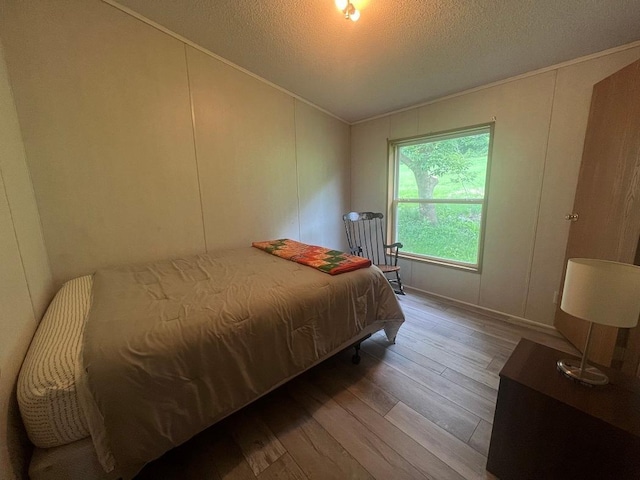 bedroom with wood finished floors, vaulted ceiling, crown molding, a textured ceiling, and a decorative wall