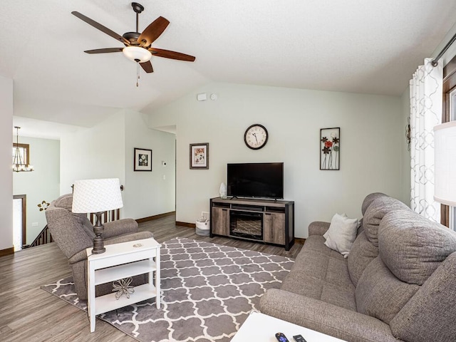 living room with vaulted ceiling, ceiling fan with notable chandelier, wood finished floors, and baseboards