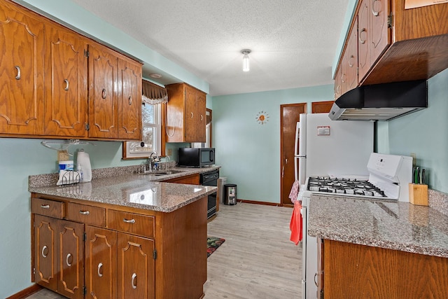 kitchen with a textured ceiling, light wood-style flooring, a sink, brown cabinets, and black appliances