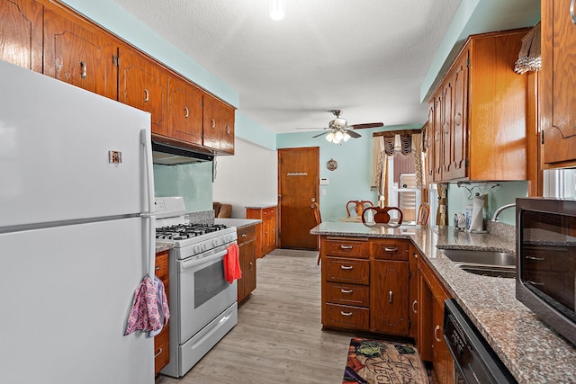 kitchen with brown cabinetry, a sink, a peninsula, white appliances, and under cabinet range hood