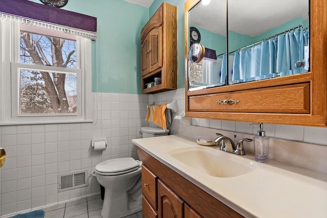 bathroom featuring visible vents, toilet, tile patterned floors, vanity, and tile walls