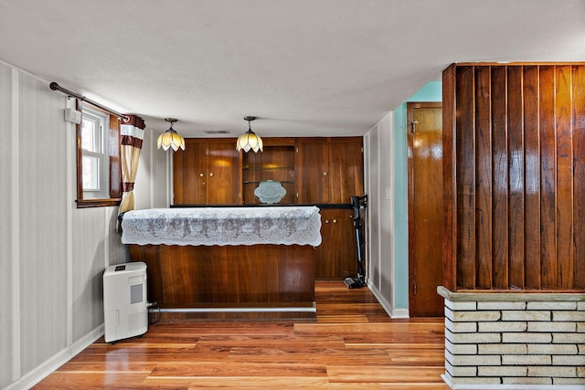 interior space with light wood-style floors, visible vents, pendant lighting, and a textured ceiling