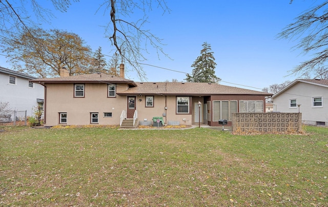 back of property with stucco siding, a chimney, fence, and a yard