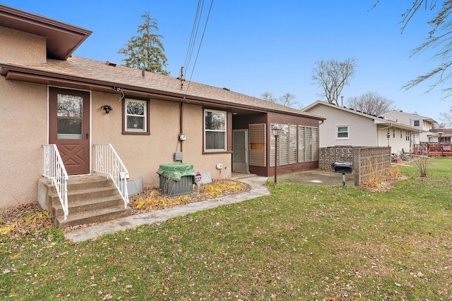 back of house featuring roof with shingles, a yard, and stucco siding