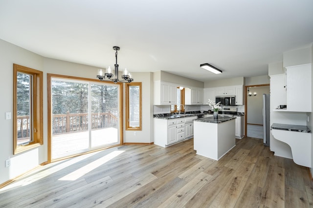 kitchen with light wood-style flooring, stainless steel appliances, white cabinetry, dark countertops, and a notable chandelier