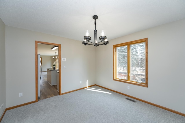 spare room featuring baseboards, carpet, visible vents, and a chandelier