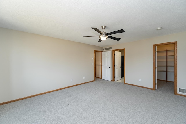 unfurnished bedroom with a spacious closet, visible vents, baseboards, and ceiling fan