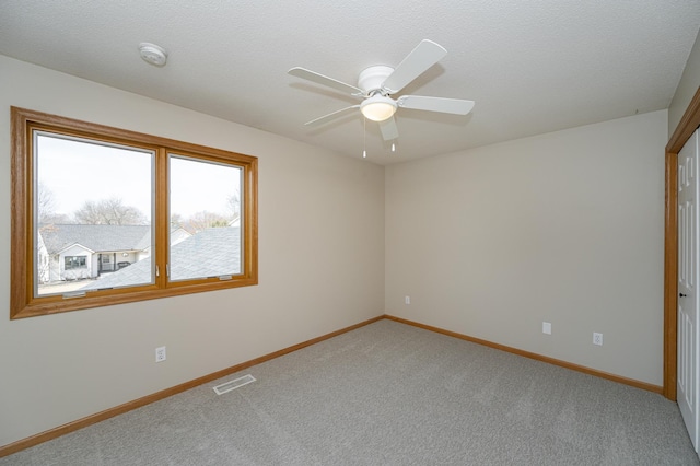 carpeted spare room with a textured ceiling, a ceiling fan, visible vents, and baseboards