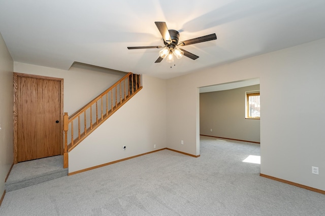 carpeted empty room with stairs, baseboards, and ceiling fan