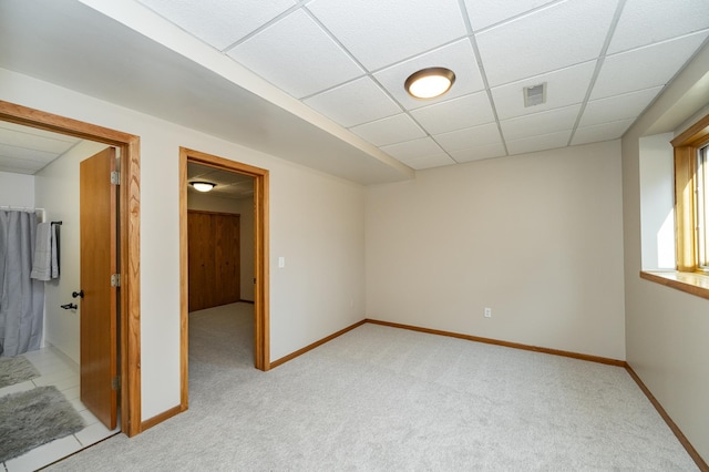 spare room featuring light carpet, visible vents, a paneled ceiling, and baseboards