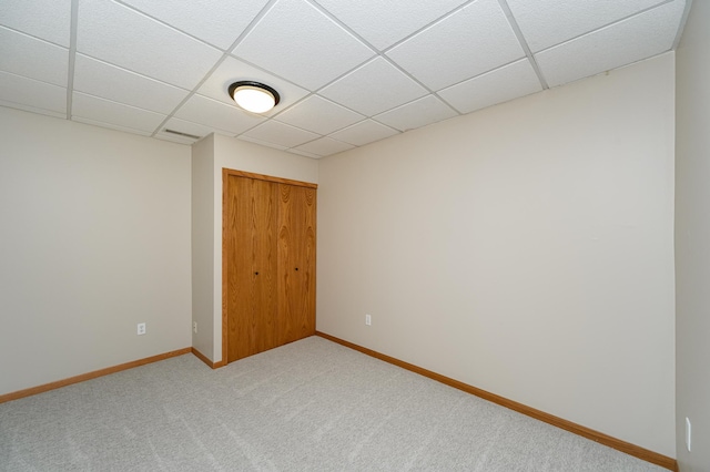 unfurnished bedroom with light carpet, a closet, a paneled ceiling, and baseboards