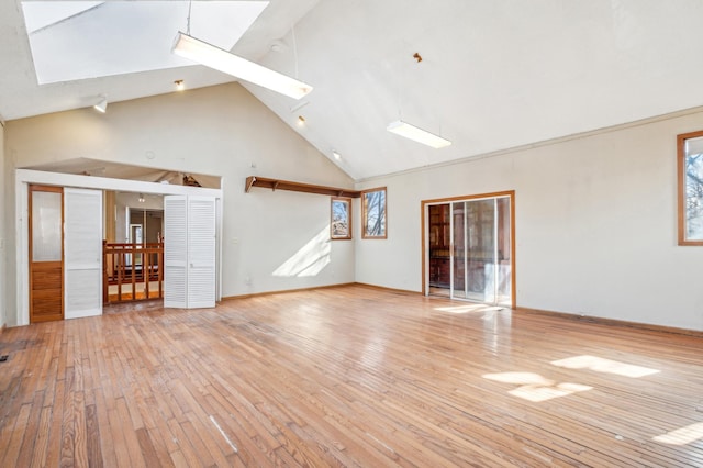 unfurnished living room featuring light wood-style floors, a skylight, high vaulted ceiling, and baseboards