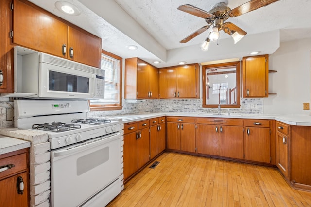 kitchen featuring white appliances, a sink, light countertops, light wood finished floors, and brown cabinetry