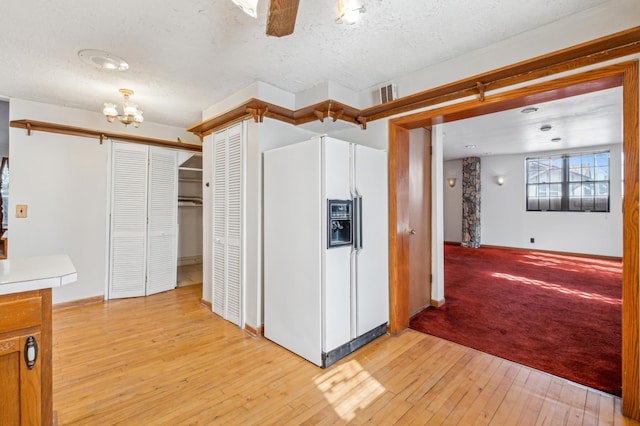 kitchen featuring a textured ceiling, white fridge with ice dispenser, light wood-type flooring, and visible vents