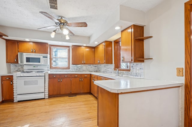 kitchen with brown cabinets, light countertops, light wood-style flooring, white appliances, and a peninsula