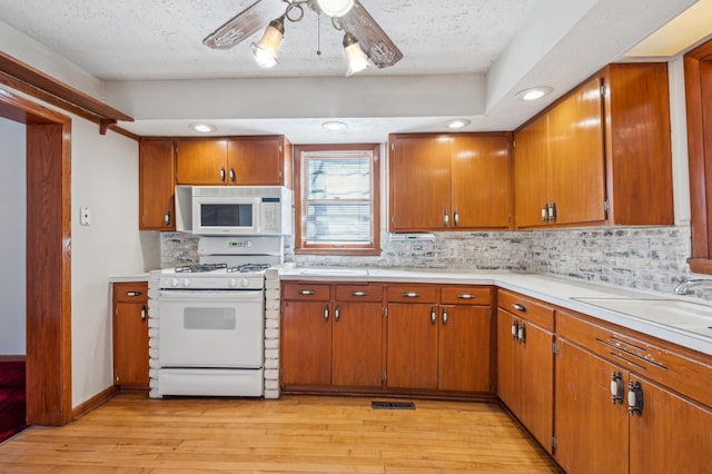 kitchen with light wood-style flooring, white appliances, light countertops, decorative backsplash, and brown cabinetry