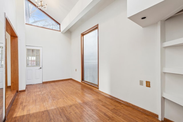 foyer with light wood-type flooring, a towering ceiling, a wealth of natural light, and a notable chandelier