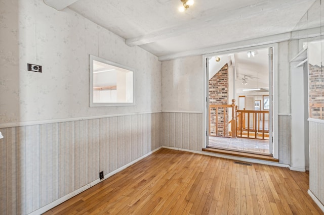 unfurnished room with vaulted ceiling with beams, light wood-style flooring, a wainscoted wall, visible vents, and wallpapered walls