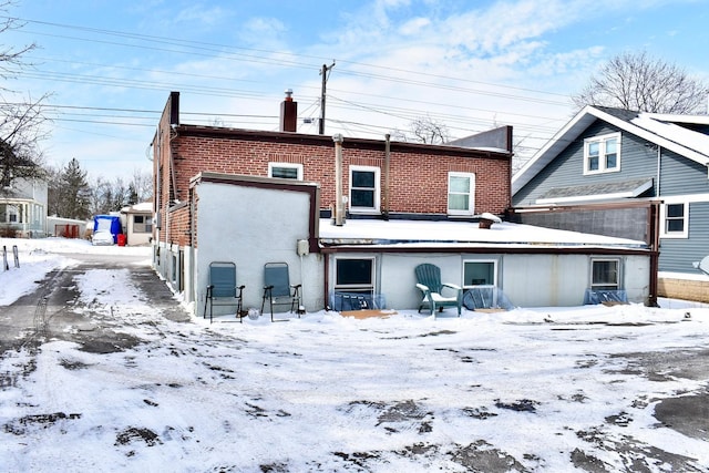 snow covered back of property featuring brick siding and a chimney