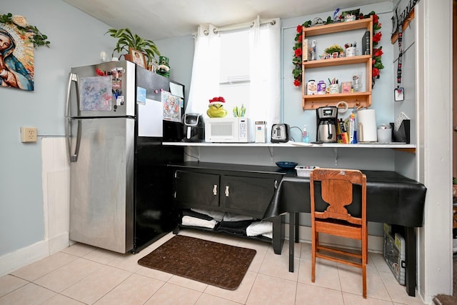 kitchen featuring white microwave, light tile patterned flooring, open shelves, and freestanding refrigerator