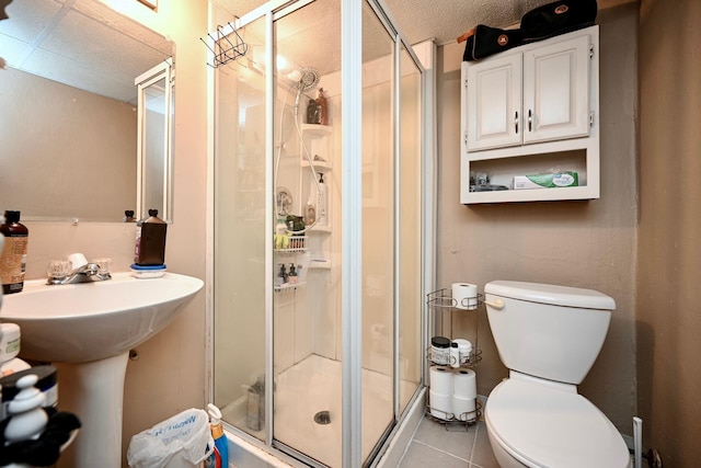 bathroom with a stall shower, a sink, toilet, and tile patterned floors