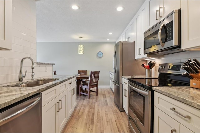 kitchen featuring light stone countertops, appliances with stainless steel finishes, white cabinets, and a sink