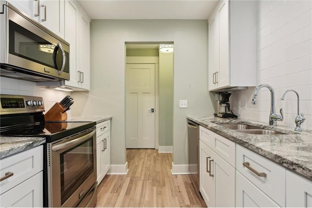 kitchen featuring stainless steel appliances, light stone counters, a sink, and white cabinets