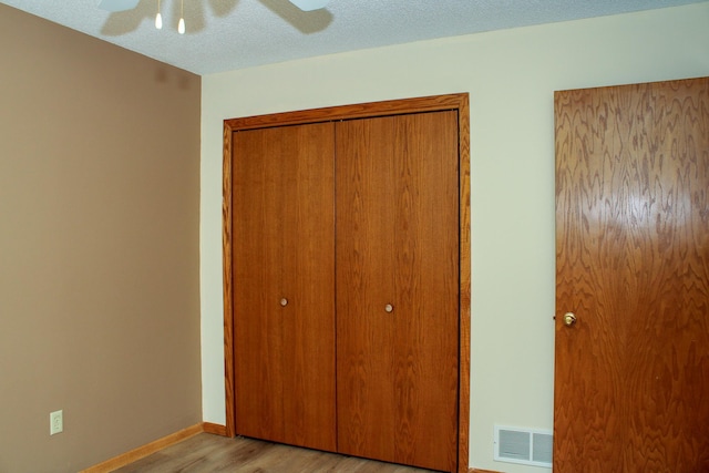 unfurnished bedroom featuring a closet, visible vents, light wood-style floors, a textured ceiling, and baseboards