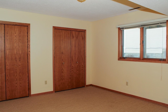 unfurnished bedroom with multiple closets, light carpet, a textured ceiling, and baseboards