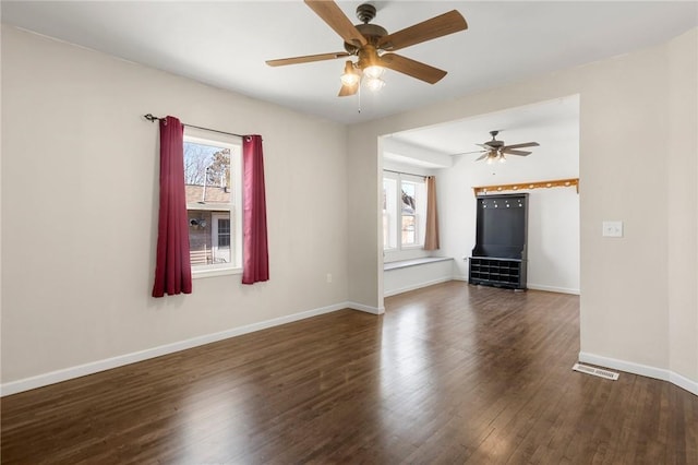 unfurnished room featuring visible vents, dark wood finished floors, a wealth of natural light, and baseboards