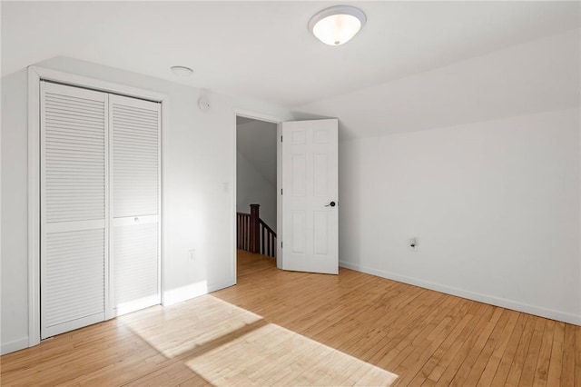 unfurnished bedroom featuring lofted ceiling, light wood-style flooring, baseboards, and a closet