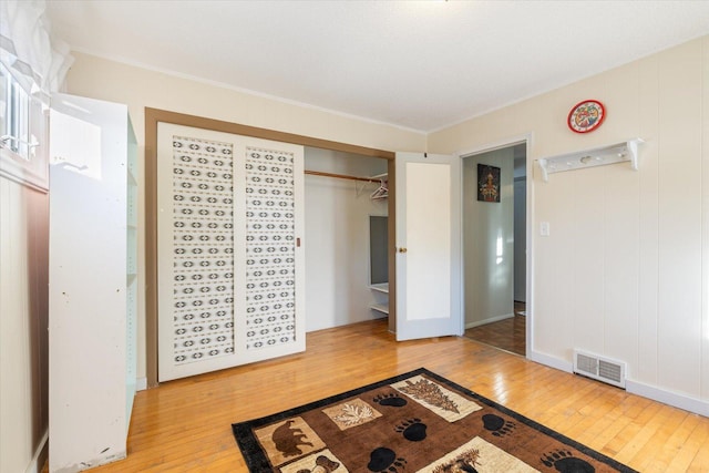 bedroom with wood-type flooring, crown molding, visible vents, and a closet