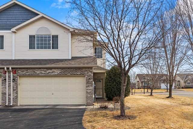 view of front of house with driveway, roof with shingles, an attached garage, and brick siding