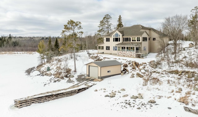 snow covered rear of property featuring a garage and an outbuilding