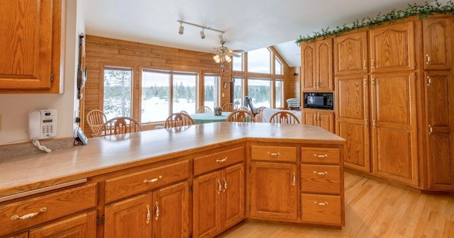 kitchen with lofted ceiling, brown cabinets, light countertops, light wood-style floors, and black microwave