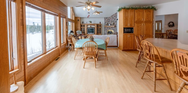 dining space with light wood-type flooring, a fireplace, visible vents, and wooden walls