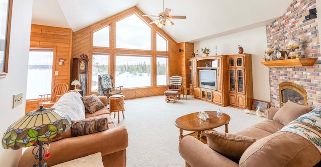 living area featuring high vaulted ceiling, carpet floors, wood walls, a ceiling fan, and a brick fireplace