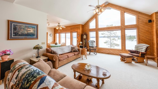 carpeted living area with high vaulted ceiling, wood walls, and a ceiling fan