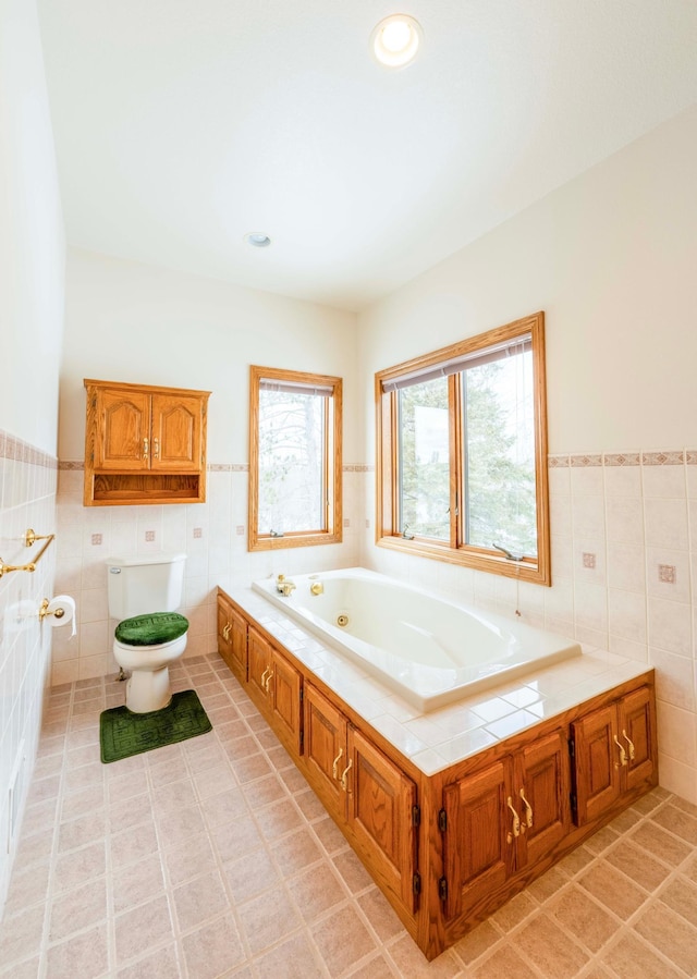 bathroom featuring toilet, a tub with jets, wainscoting, and tile walls